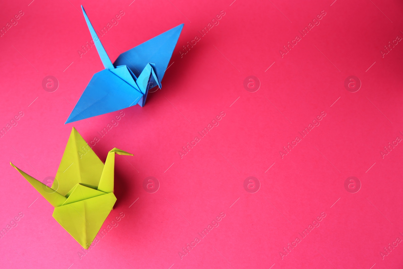 Photo of Origami art. Colorful handmade paper cranes on pink background, above view. Space for text