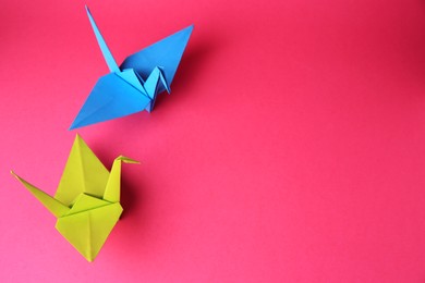 Origami art. Colorful handmade paper cranes on pink background, above view. Space for text