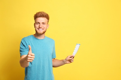 Portrait of happy young man with lottery ticket on yellow background