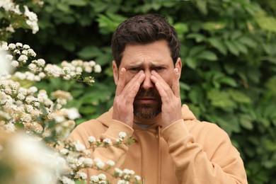 Photo of Man suffering from seasonal pollen allergy near blossoming tree on spring day