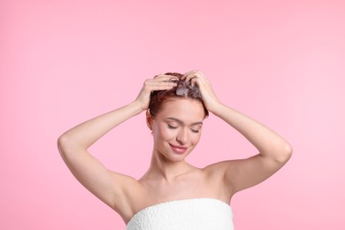 Happy young woman washing her hair with shampoo on pink background