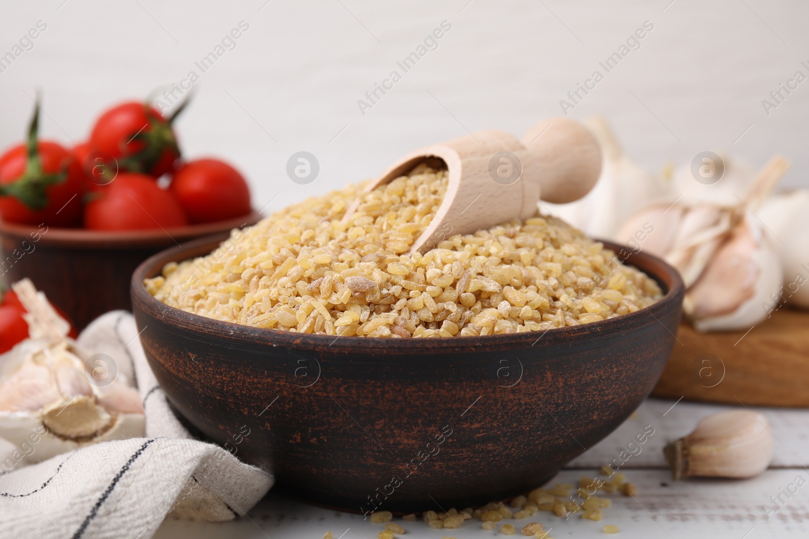 Photo of Bowl and scoop with raw bulgur on white wooden table, closeup