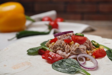 Photo of Delicious tortilla with tuna and vegetables on table, closeup. Cooking shawarma