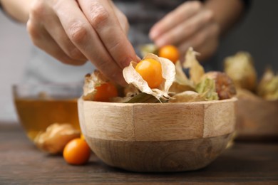 Woman peeling physalis fruit from calyxes at wooden table, closeup