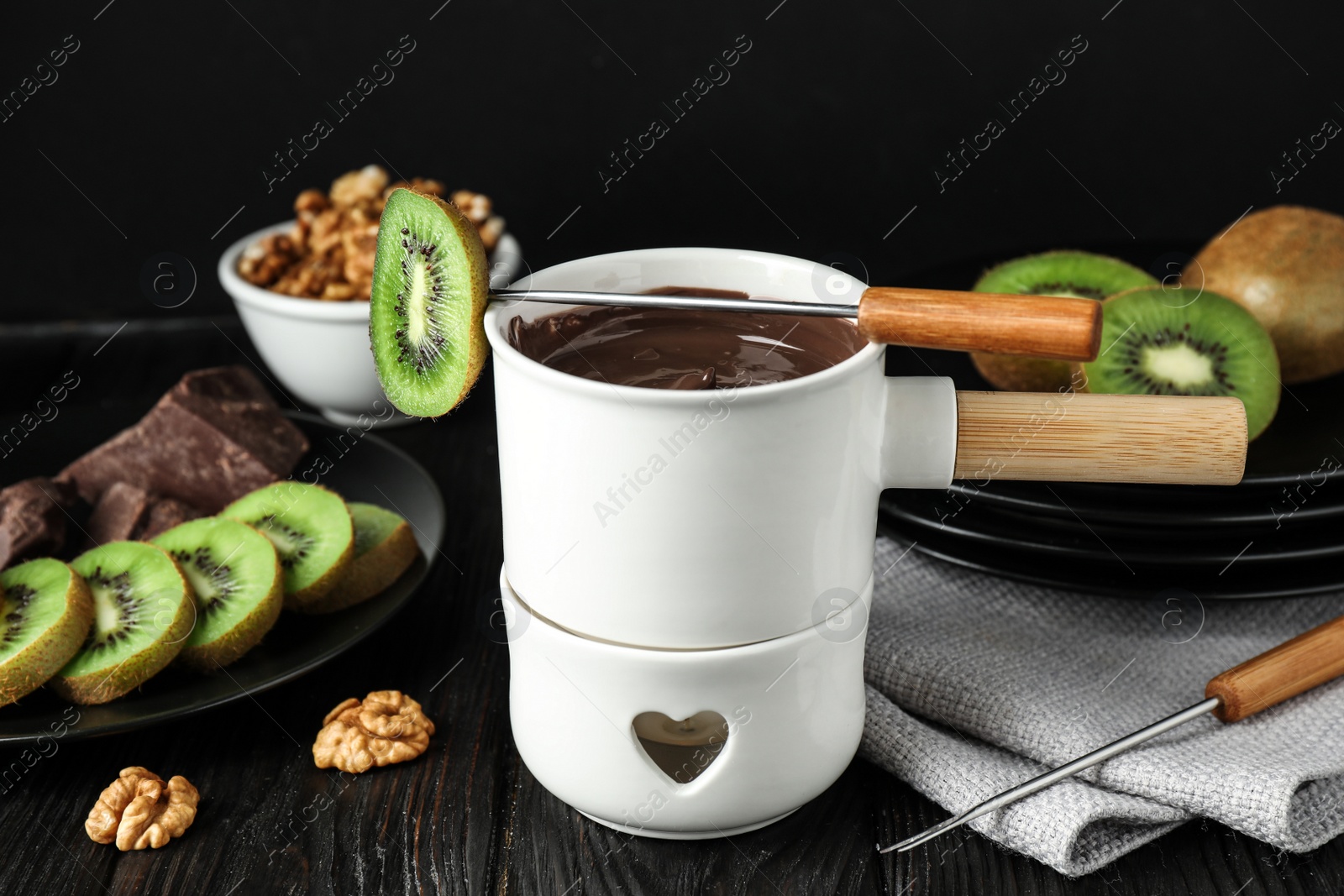 Photo of Fondue pot with chocolate and kiwis on black wooden table