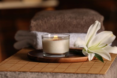 Photo of Spa composition with burning candle, lily flower and towels on massage table in wellness center