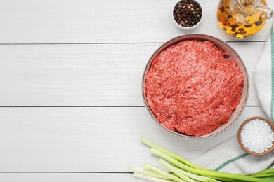 Photo of Bowl of raw fresh minced meat and ingredients on white wooden table, flat lay. Space for text