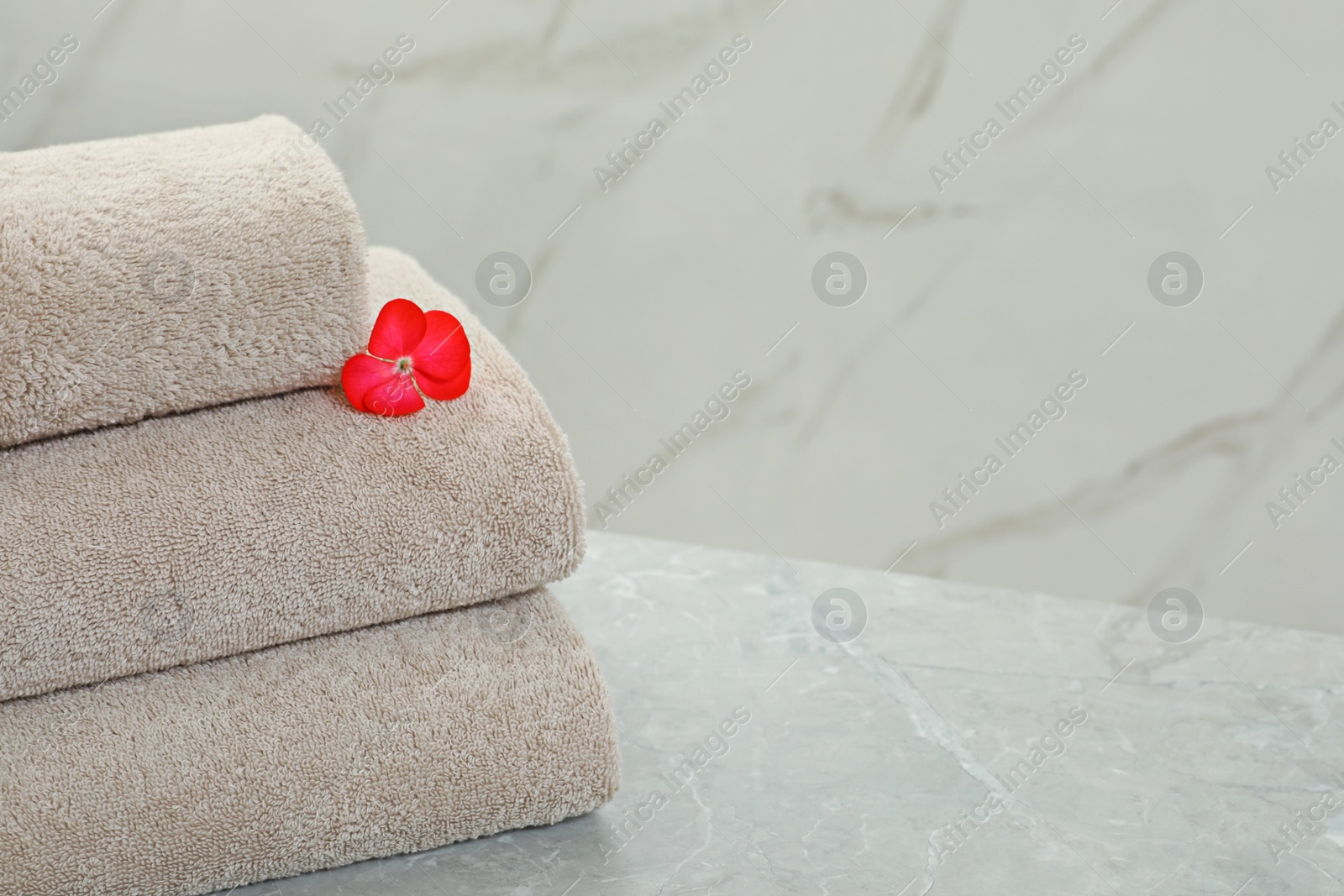 Photo of Stack of fresh towels with flower on grey table against light background. Space for text