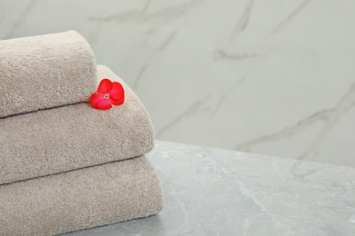 Stack of fresh towels with flower on grey table against light background. Space for text