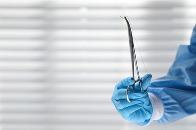 Photo of Doctor holding needle with suture thread indoors, closeup and space for text. Medical equipment