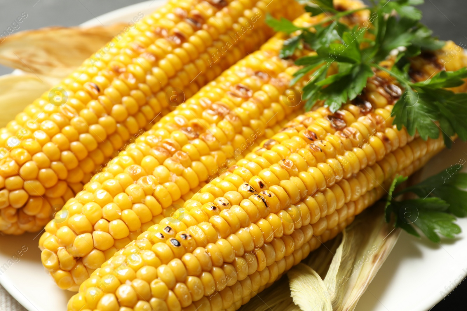 Photo of Tasty grilled corn with parsley, closeup view