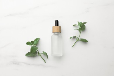 Bottle of mint essential oil and fresh herb on white marble table, flat lay