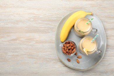 Photo of Tasty banana smoothie and ingredients on white wooden table, flat lay. Space for text