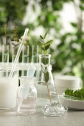 Photo of Natural ingredients for cosmetic products and laboratory glassware on grey table against blurred green background