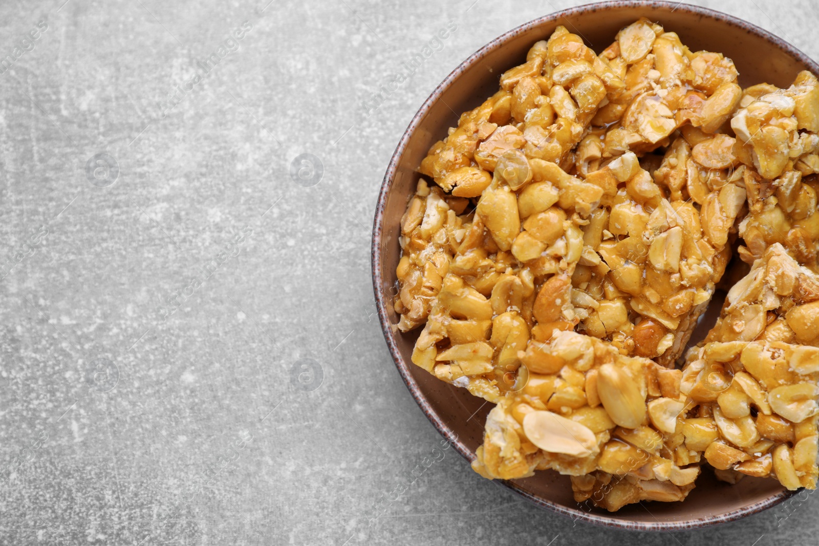 Photo of Bowl with delicious peanut kozinaki bars on light gray textured table, top view. Space for text