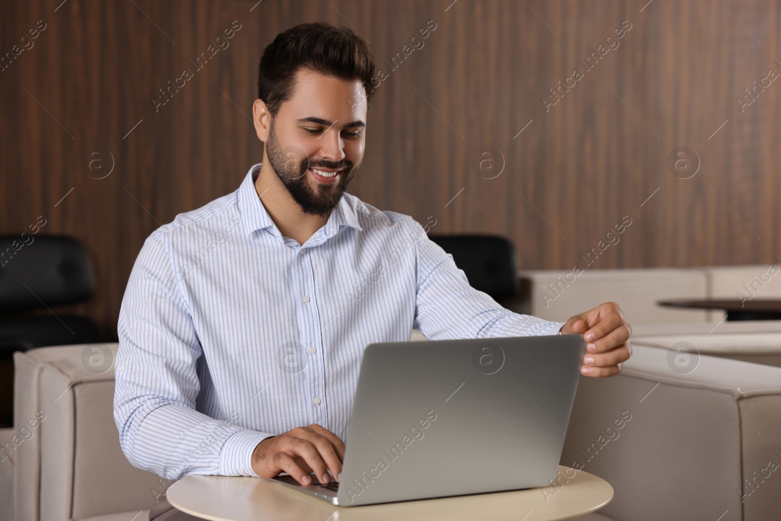 Photo of Happy young man working on laptop at table in office