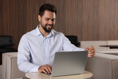 Happy young man working on laptop at table in office