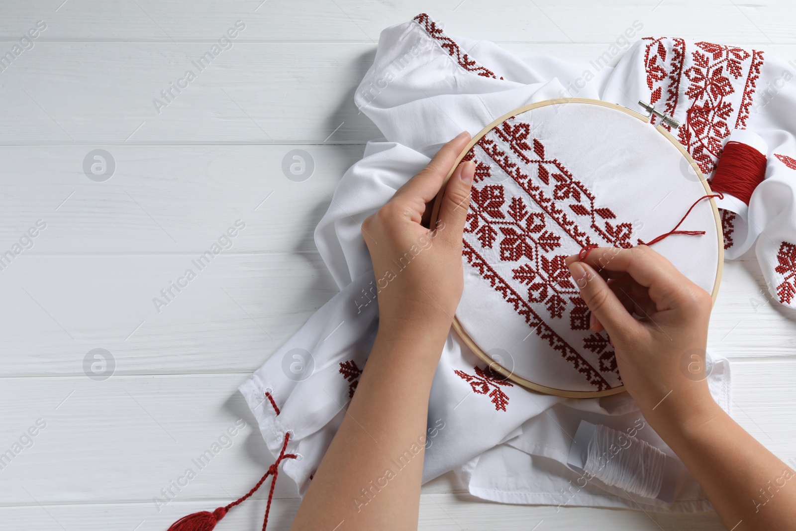 Photo of Woman embroidering shirt with red thread at white wooden table, top view and space for text. Ukrainian national clothes