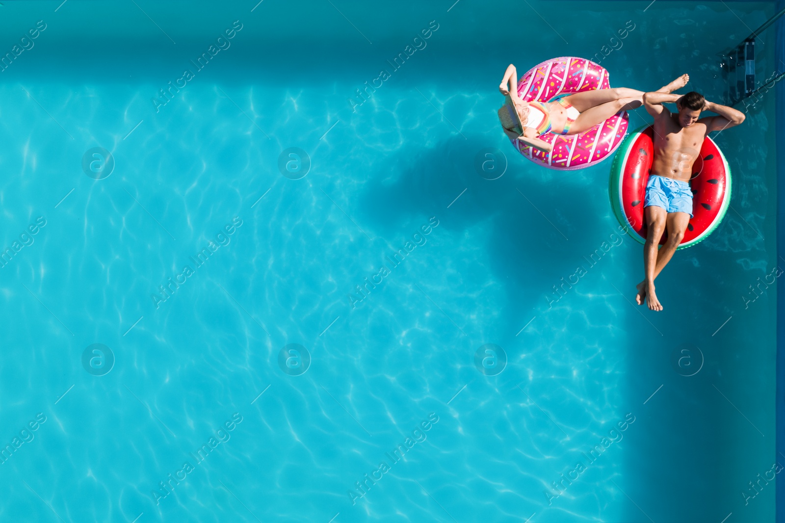 Image of Happy couple with inflatable rings in swimming pool, top view and space for text. Summer vacation