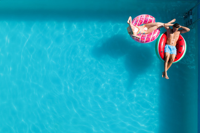 Image of Happy couple with inflatable rings in swimming pool, top view and space for text. Summer vacation