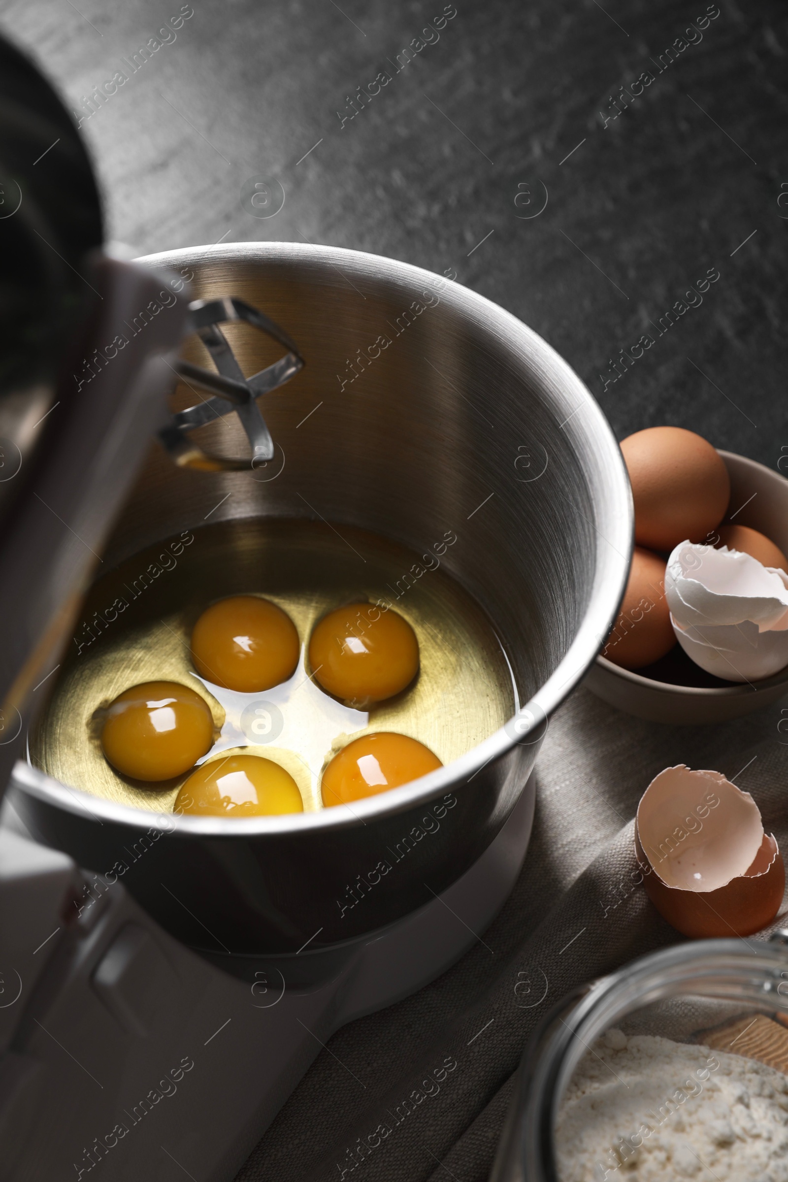 Photo of Making dough. Raw eggs in bowl of stand mixer and ingredients on black table, closeup