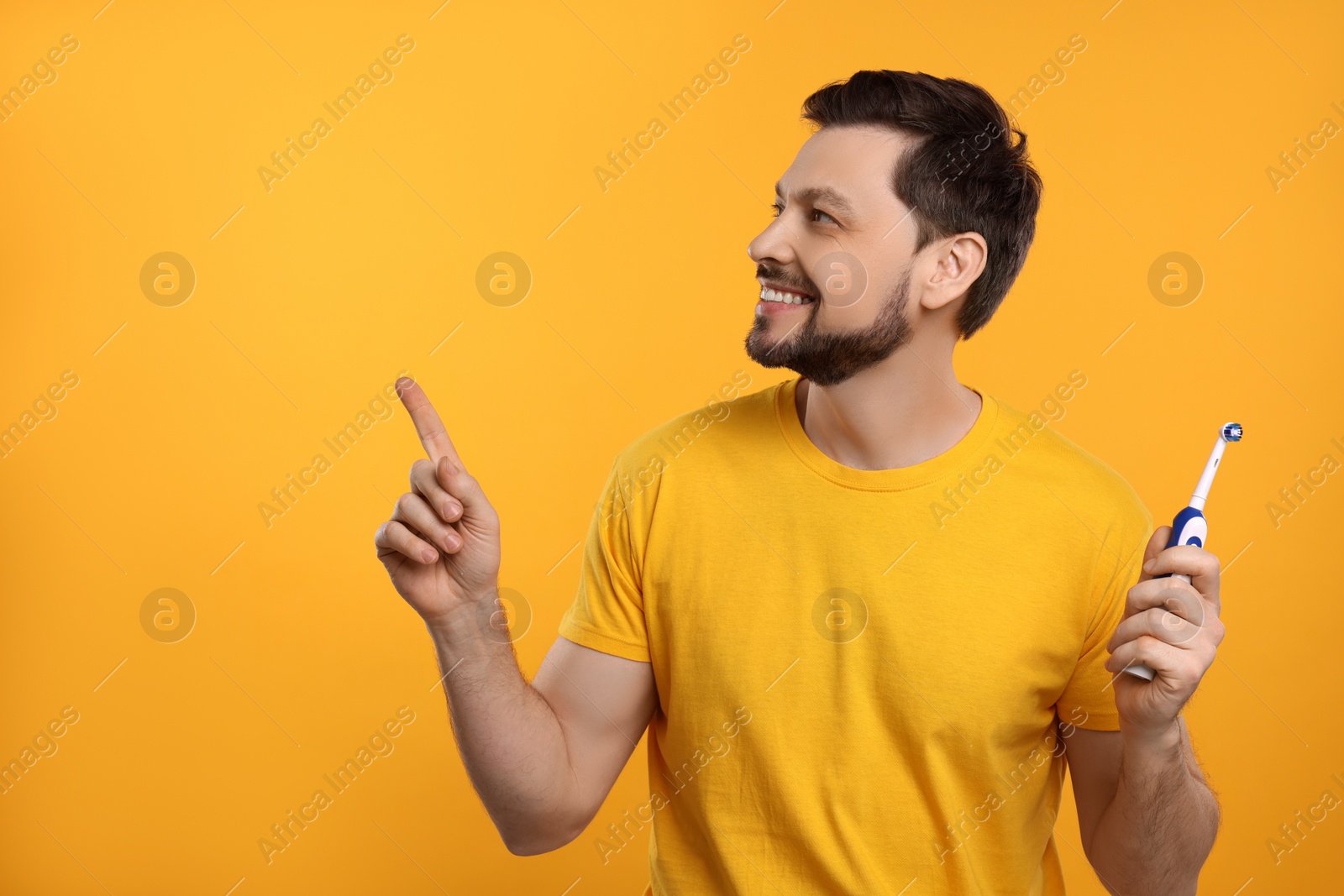 Photo of Happy man holding electric toothbrush on yellow background. Space for text