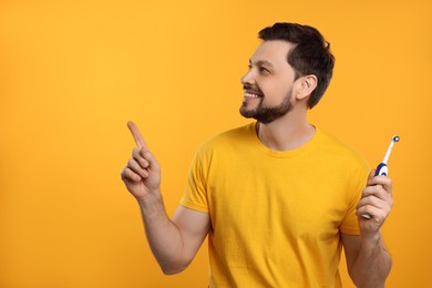 Photo of Happy man holding electric toothbrush on yellow background. Space for text