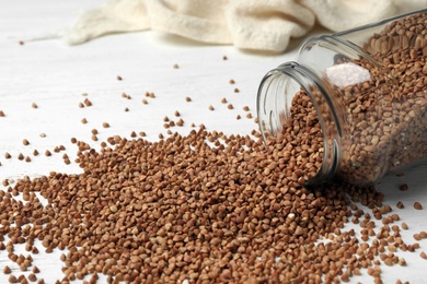 Overturned glass jar with uncooked buckwheat on table