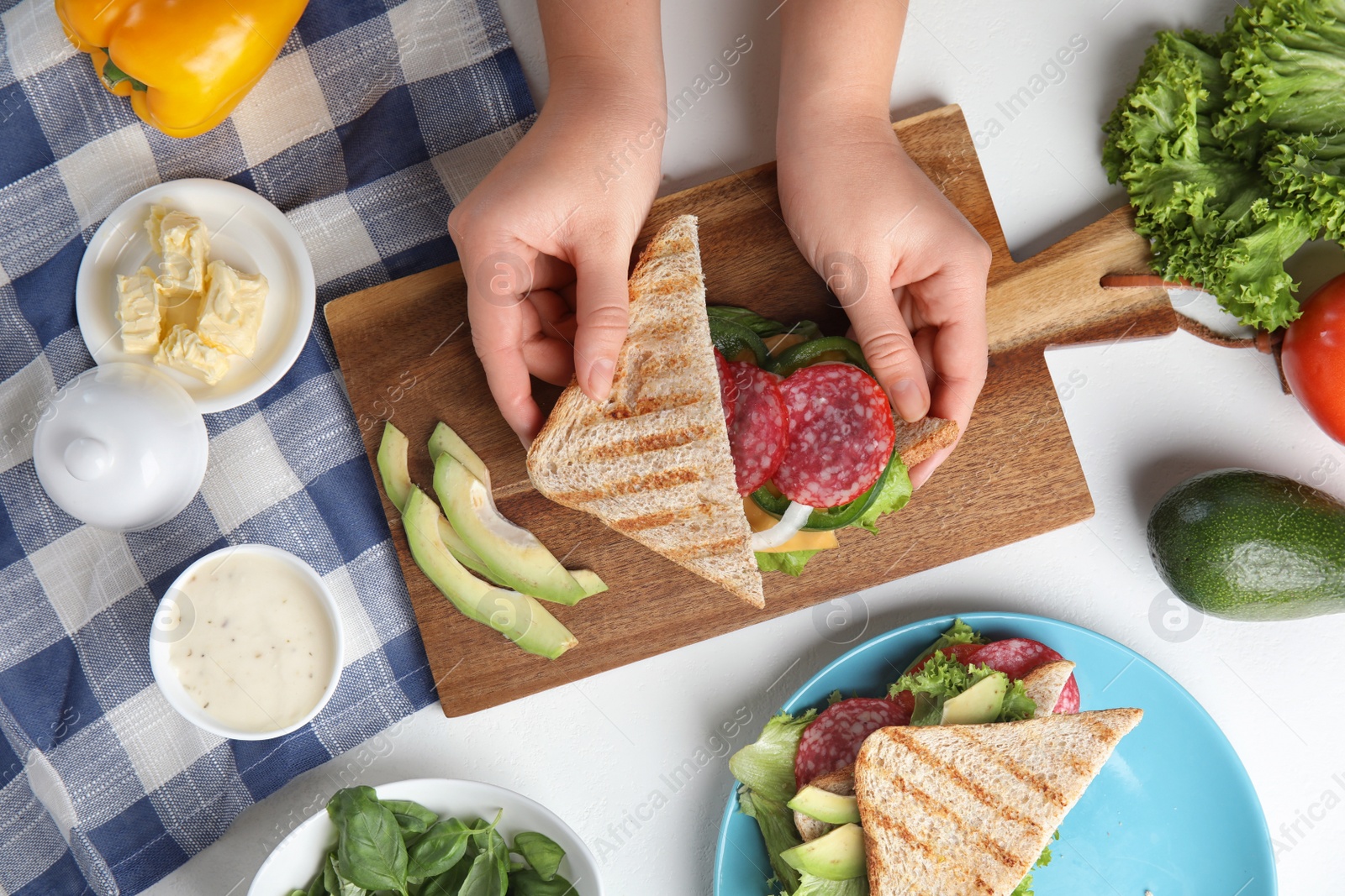 Photo of Woman making tasty sandwich with sausage at white table, top view