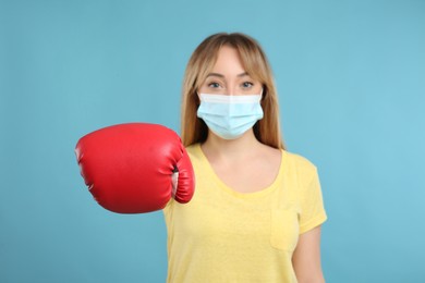 Photo of Woman with protective mask and boxing gloves on light blue background. Strong immunity concept