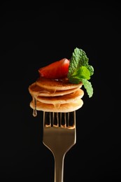 Photo of Fork with cereal pancakes, strawberry and mint on black background