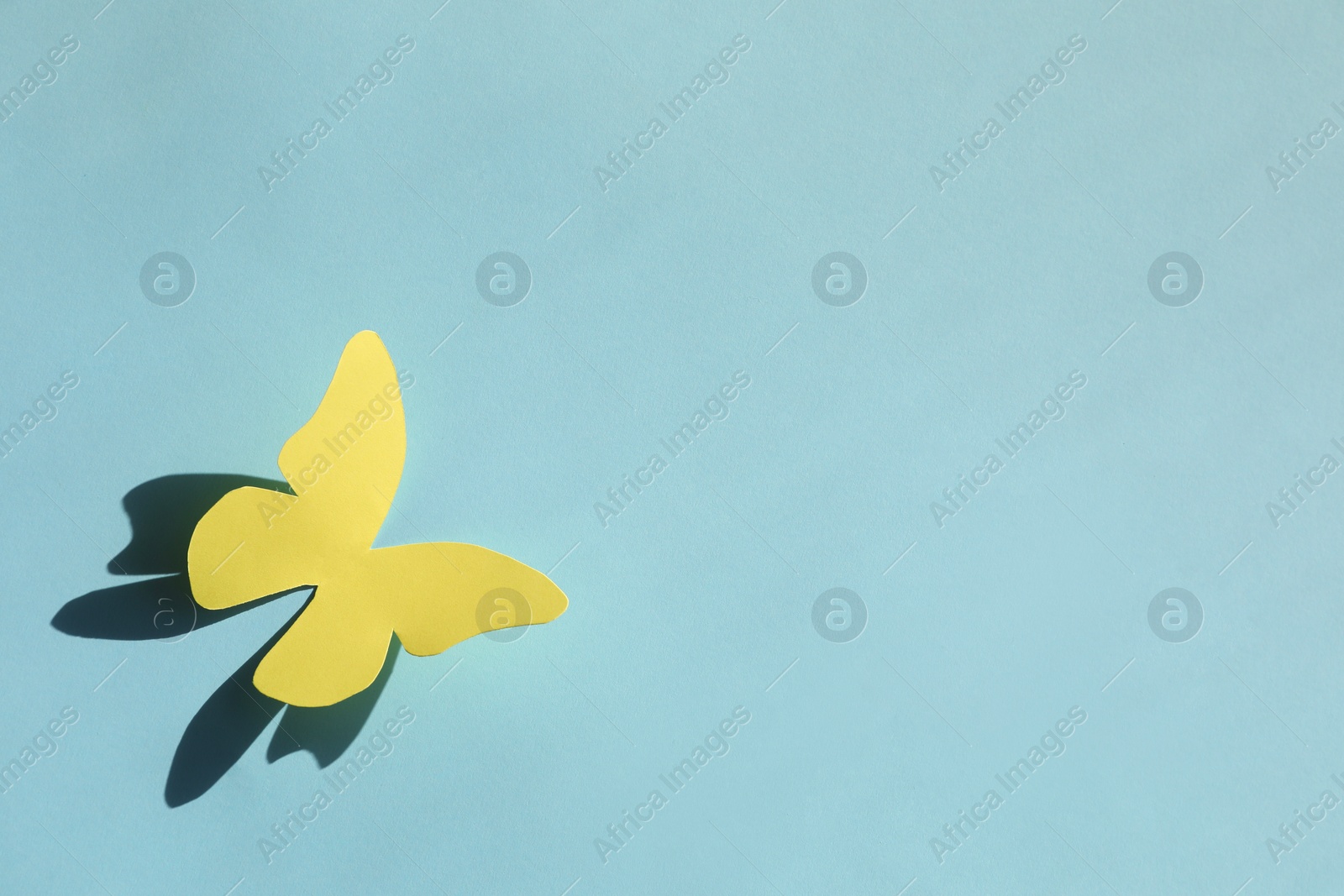 Photo of Yellow paper butterfly on turquoise background, top view. Space for text