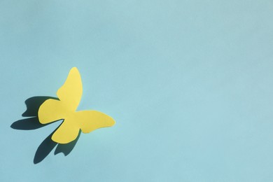 Photo of Yellow paper butterfly on turquoise background, top view. Space for text