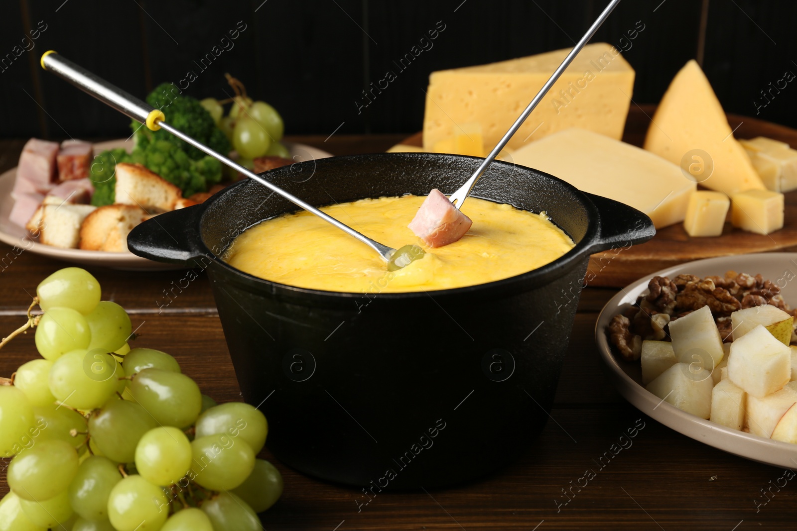 Photo of Fondue pot with melted cheese, forks and different products on wooden table, closeup