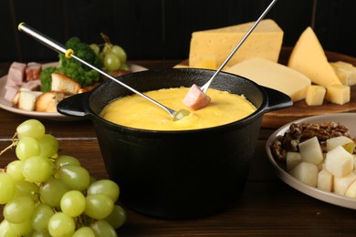 Photo of Fondue pot with melted cheese, forks and different products on wooden table, closeup