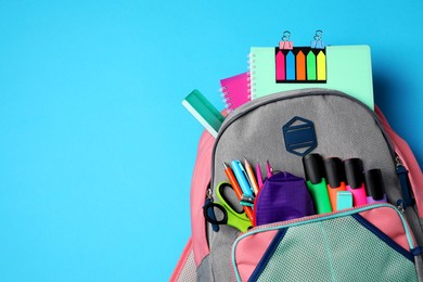 Photo of Backpack with school stationery on light blue background, top view. Space for text