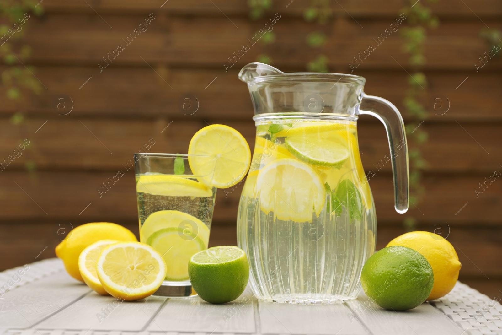 Photo of Water with lemons and limes on white wooden table outdoors