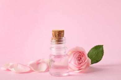 Photo of Bottle of essential oil and rose on pink background