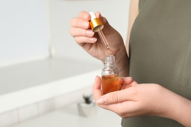 Woman with pipette and bottle of essential oil indoors, closeup. Space for text