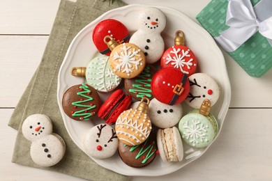 Photo of Beautifully decorated Christmas macarons and gift box on white wooden table, flat lay