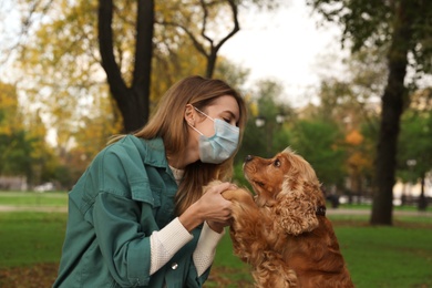 Photo of Woman in protective mask with English Cocker Spaniel in park. Walking dog during COVID-19 pandemic