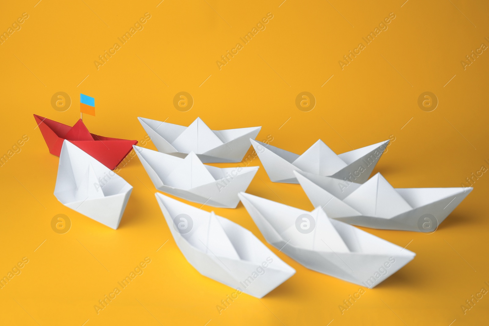 Photo of Group of paper boats following red one on yellow background. Leadership concept