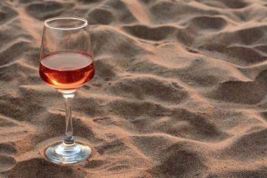 Glass of tasty rose wine on sand, space for text