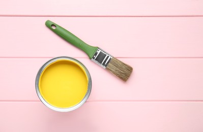 Can of yellow paint and brush on pink wooden table, flat lay. Space for text