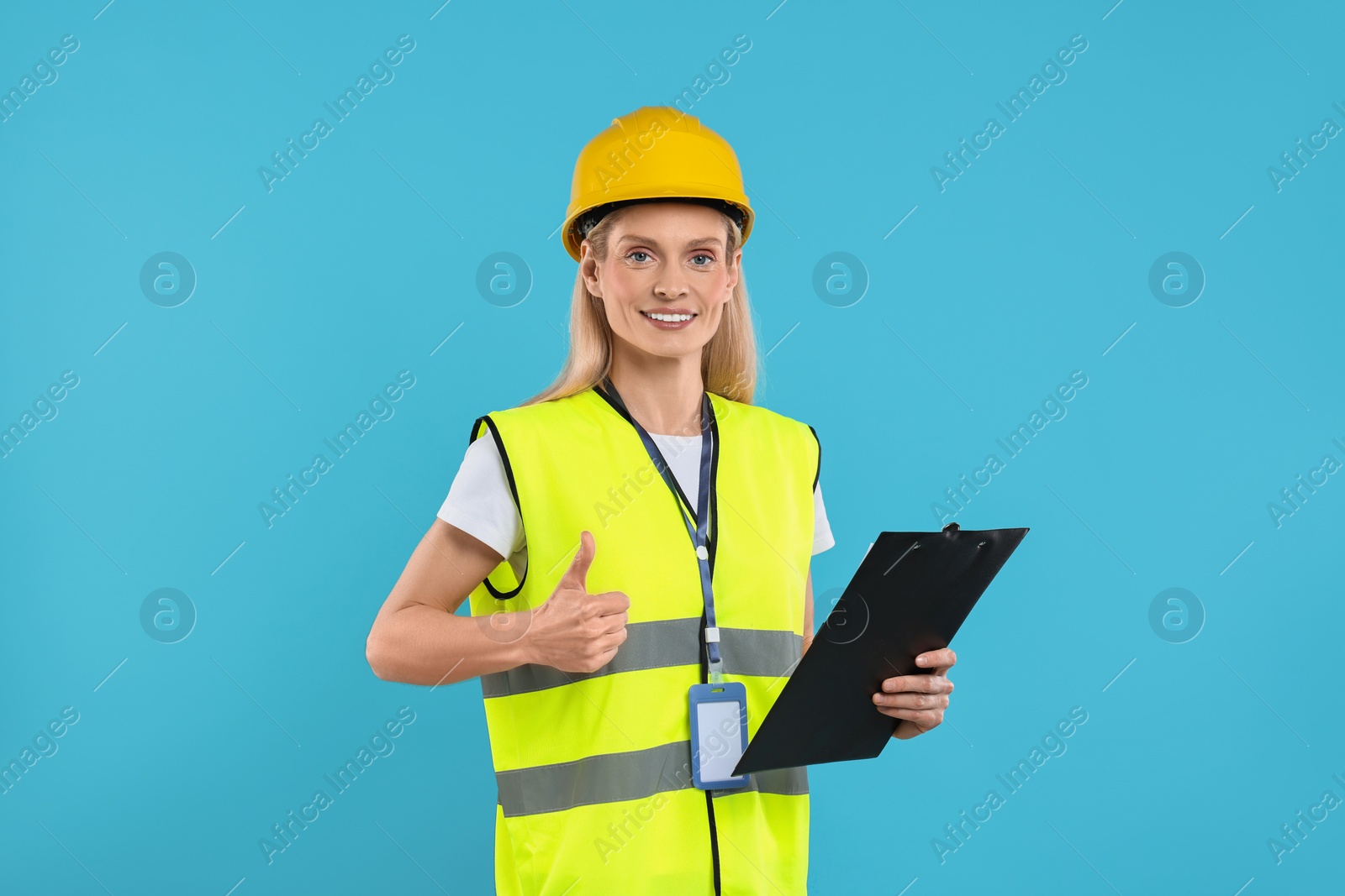 Photo of Engineer in hard hat holding clipboard and showing thumb up on light blue background