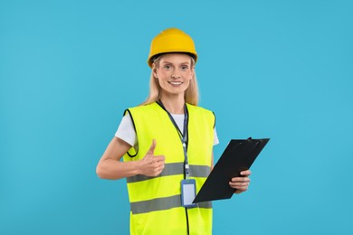 Photo of Engineer in hard hat holding clipboard and showing thumb up on light blue background
