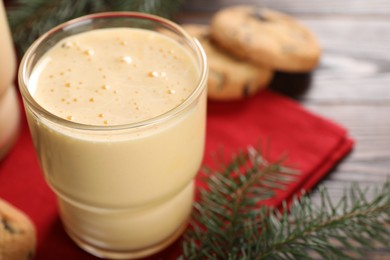 Tasty eggnog, cookies and fir branches on wooden table, closeup