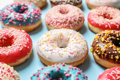 Delicious glazed doughnuts with sprinkles on color background