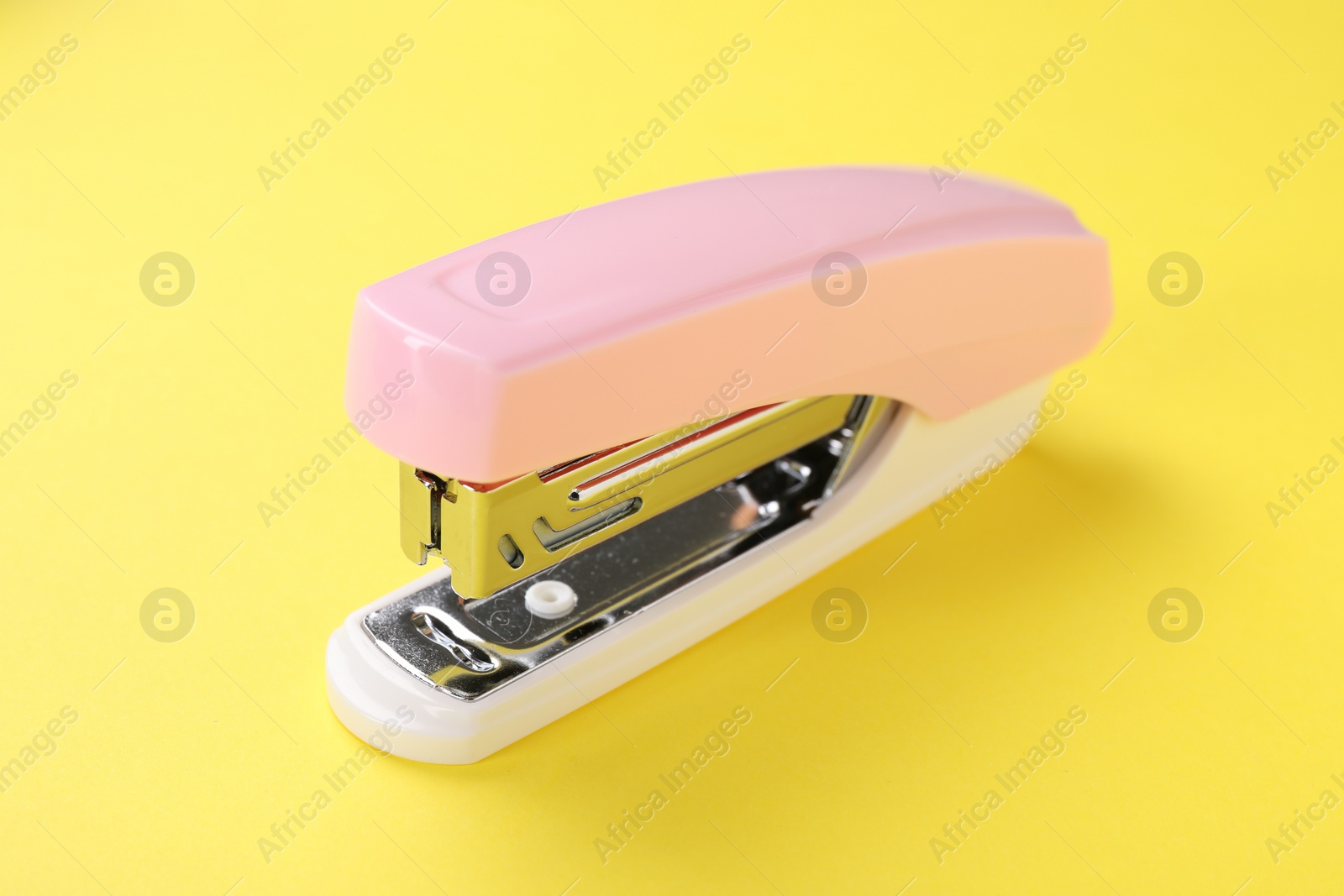 Photo of One pink stapler on yellow background, closeup