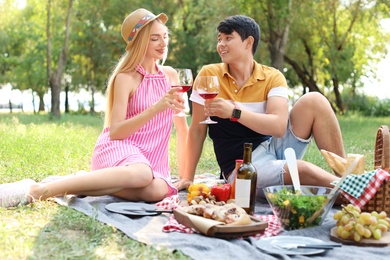 Photo of Happy couple with glasses of wine sitting on lawn. Summer picnic